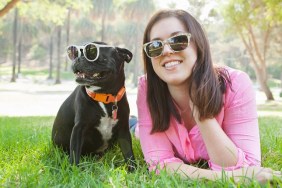 Portrait of young woman and dog lying in park wearing sunglasses