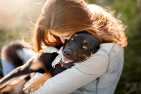 A woman hugging her new cute black mutt dog who was just up for adoption