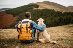 Man resting on top of mountain with dog after a hike